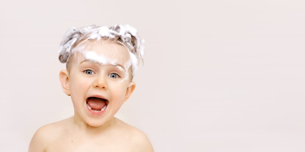 Schattig jongetje met shampoo in zijn haar in een kinderbadkamer